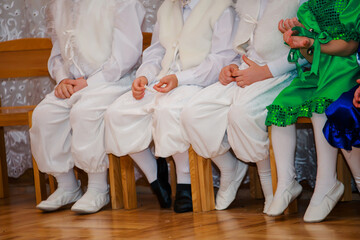 Children sit on a chair on children. Boys dressed in costumes rabbits. Young children lay hands on lap.