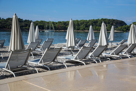 Garden design and landscaping: Comfortable sun loungers and shady parasols at a promenade with elaborate nature stone paving slabs at a pebbles beach, beautiful view to the adriatic sea,Rovinj,Croatia