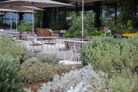 Modern garden design - Hotel restaurant cafe terrace with a mix of tables and chairs made of different materials as metal, wood, osier, surrounded by pots, green plants and herbs, blurred background