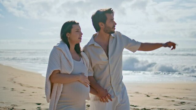 Pregnant couple enjoy sea landscape walking beach sand. Woman expecting baby