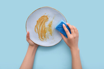 Female hands washing dirty plate with sponge on blue background