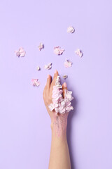 Woman with glitter and floral petals on lilac background. Hand care concept