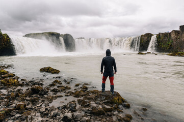 Back view of a man standing next to the river with waterfalls and watching a majestic view.
