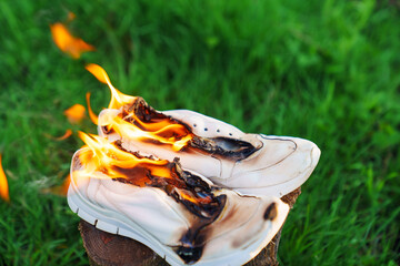 Burning leather sports shoes. Sneakers or gym shoes on fire stand on the Stump. - obrazy, fototapety, plakaty