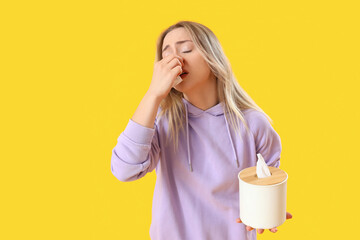 Allergic young woman with tissue box on yellow background