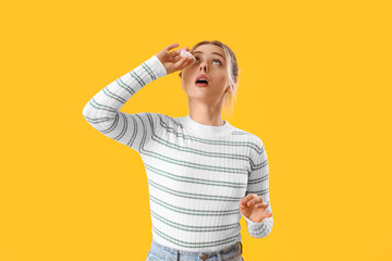 Allergic young woman with eye drops on yellow background
