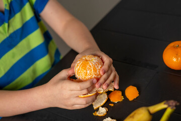 children's hands peel a tangerine over the table
