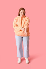Allergic young woman scratching on pink background