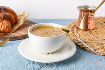 Cup of delicious espresso with jezve and croissant on blue background