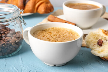 Cups of delicious espresso with coffee beans and croissant on blue background, closeup