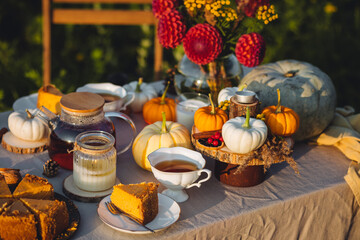 Tea setting with handmade pie. Beautiful view of garden wooden furniture with basket, soft blanket and burning candles. Outdoors fall family party, cozy autumn interior. Pumpkins, red dahlia