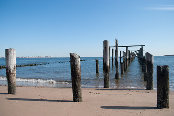 Horizon view of the ocean with wooden groynes in the water and sand. Clear blue skies. 
