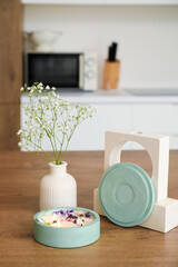Gypsophila flowers and burning candle on table in light kitchen, closeup