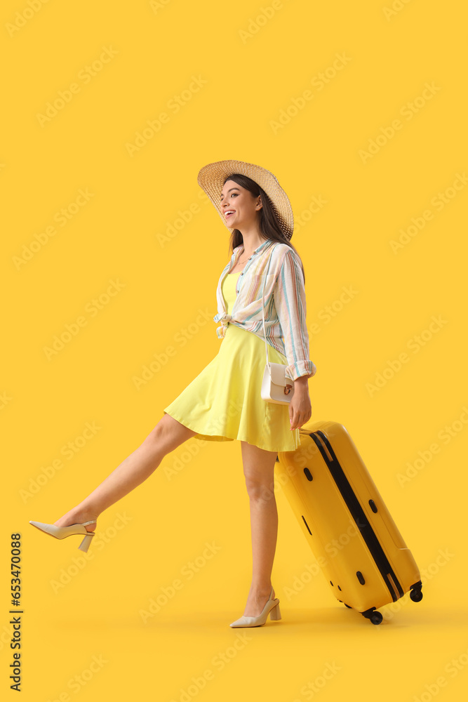 Wall mural young woman with suitcase on yellow background