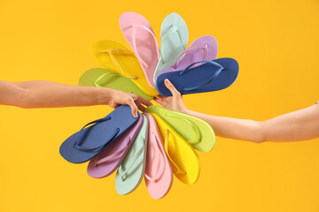 Hands with many flip-flops on yellow background