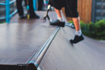 Fototapeta premium Skate park with kids on a kick scooter doing tricks and stunts, boys in a skate park riding bmx bike and skate, playing and enjoying summer on new ramp, teenagers skateboarders and bmx riders