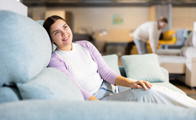 young girl sits on sofa in store and enjoys comfort of chosen sofa