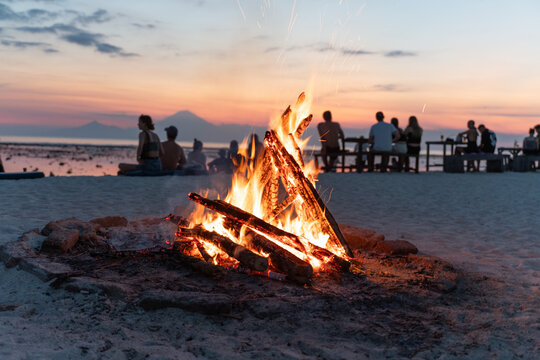 many friends enjoying a campfire in the beach at sunset