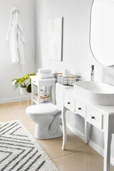 Interior of light restroom with ceramic toilet bowl and vanities