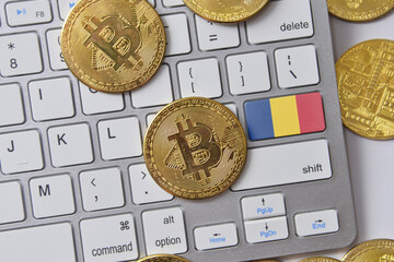 national flag of romania on the keyboard with bitcoin coins on a grey background.