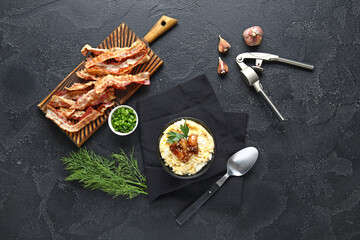 Bowl of tasty banosh and bacon on black background