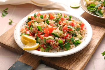 Plate with delicious tabbouleh salad on pink tile background, closeup