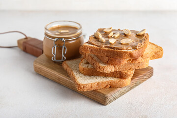 Wooden board of toasts with peanut butter and nuts on white background