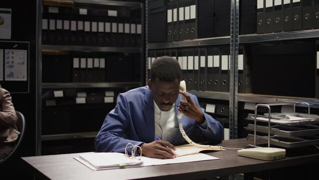 Black cop conducts a discreet investigation, analyses evidence, and makes important phone calls. African american law officer collects classified witness statements and information over the telephone.