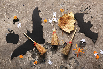 Halloween composition with brooms, bats and ghosts on grey grunge background