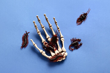 Halloween composition with candy bugs and skeleton hand on blue background