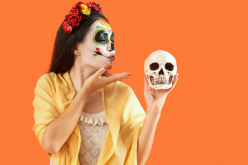 Beautiful woman dressed for Halloween with painted skull blowing kiss on orange background