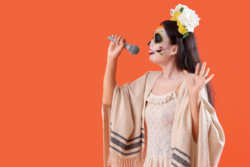 Beautiful woman dressed for Halloween with microphone singing on orange background