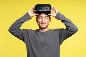 Professional asian gamer wearing VR glasses playing video game, isolated on yellow background