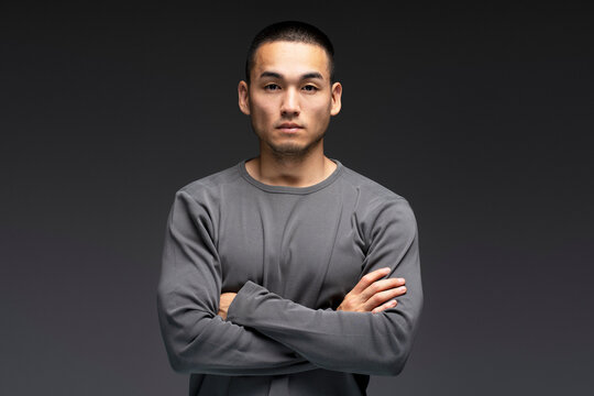Serious, emotionless young Asian man standing isolated on black background, looking at camera