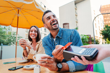 Happy young adult man paying the bill with a contactless credit card on a restaurant, bar or coffee...