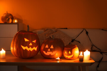 Halloween pumpkins with burning candles on table in dark living room