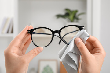 Woman wiping her glasses with microfiber cloth at home, closeup