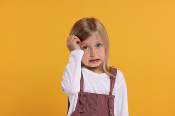 Portrait of embarrassed little girl on orange background - obrazy, fototapety, plakaty