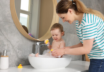 Mother washing her little baby in sink at home