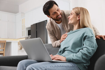 Happy couple using laptop on sofa at home, low angle view