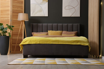 Large comfortable bed, lamp and green houseplant in stylish room. Bedroom interior