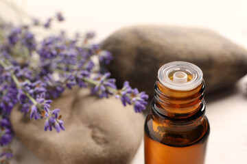 Bottle of essential oil and lavender flowers on white table, closeup. Space for text