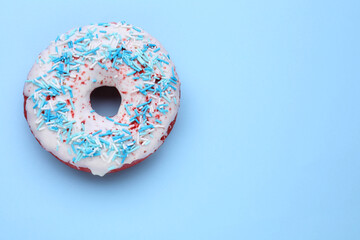 Glazed donut decorated with sprinkles on light blue background, top view. Space for text. Tasty confectionery