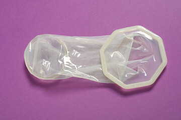Unrolled female condom on violet background, closeup. Safe sex
