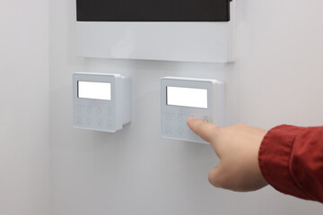 Man adjusting thermostat on white wall, closeup. Smart home system