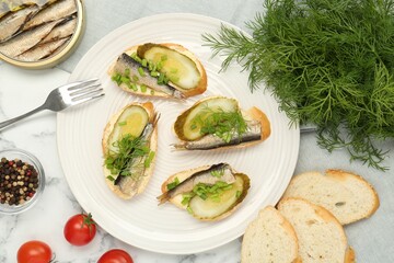 Delicious sandwiches with sprats, pickled cucumber, green onion and dill served on white marble table, flat lay