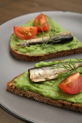 Delicious sandwiches with sprats, tomatoes, avocado puree and dill on table, closeup