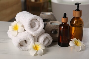 Fototapeta na wymiar Spa products, burning candles, towels and plumeria flowers on white table in bathroom, closeup