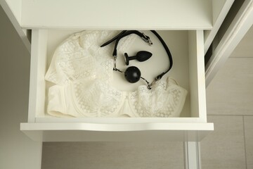 Anal plug, ball gag and women's underwear in open drawer of nightstand indoors, above view. Sex toys