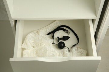 Anal plug, ball gag and women's underwear in open drawer of nightstand indoors, closeup. Sex toys - obrazy, fototapety, plakaty